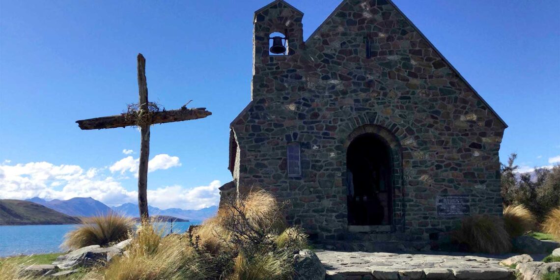 photo of wooden Christian cross outside small stone church building