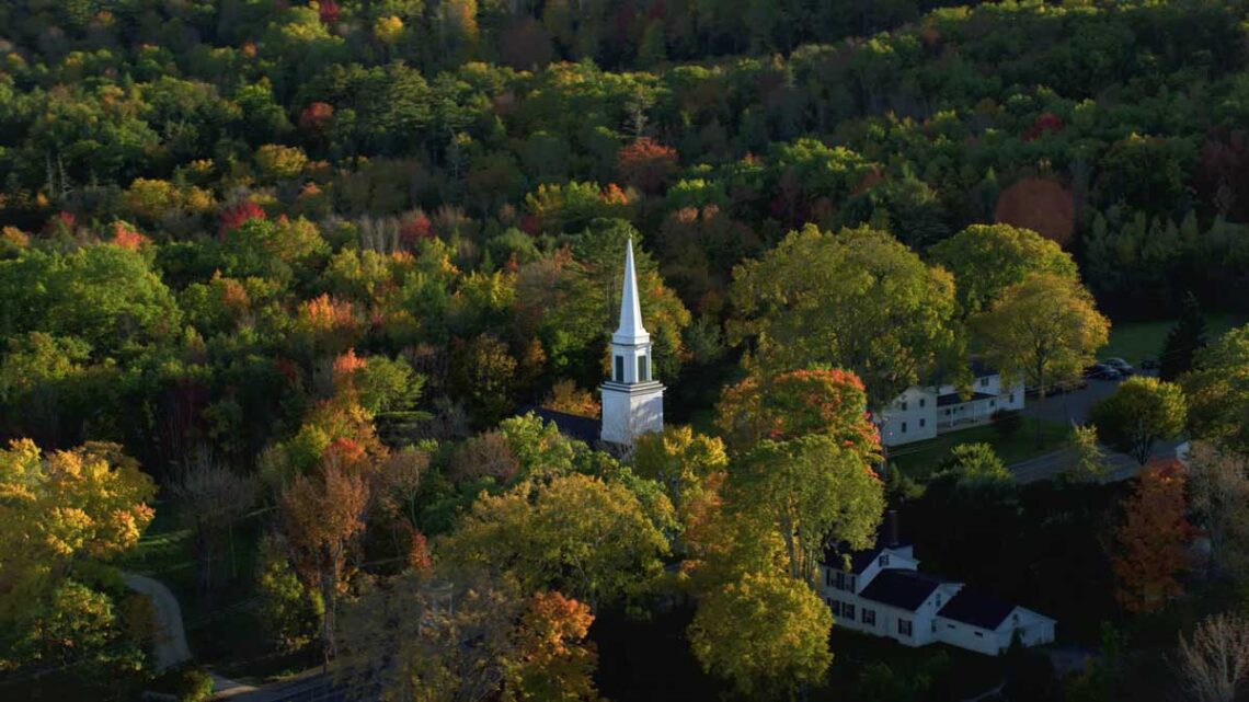 Photo of a white church steeple against autumn foliage in Maine