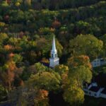 Photo of a white church steeple against autumn foliage in Maine