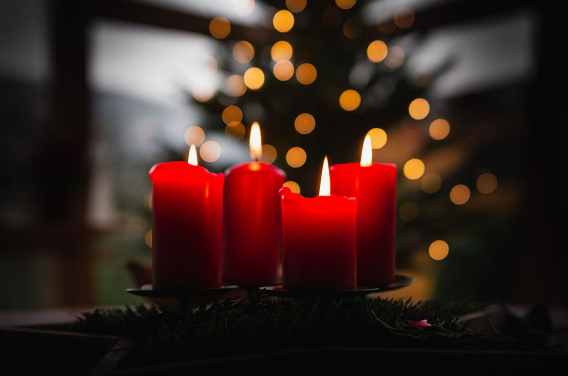Photo of lit red Advent candles in front of blurry Christmas tree and lights
