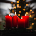 Photo of lit red Advent candles in front of blurry Christmas tree and lights