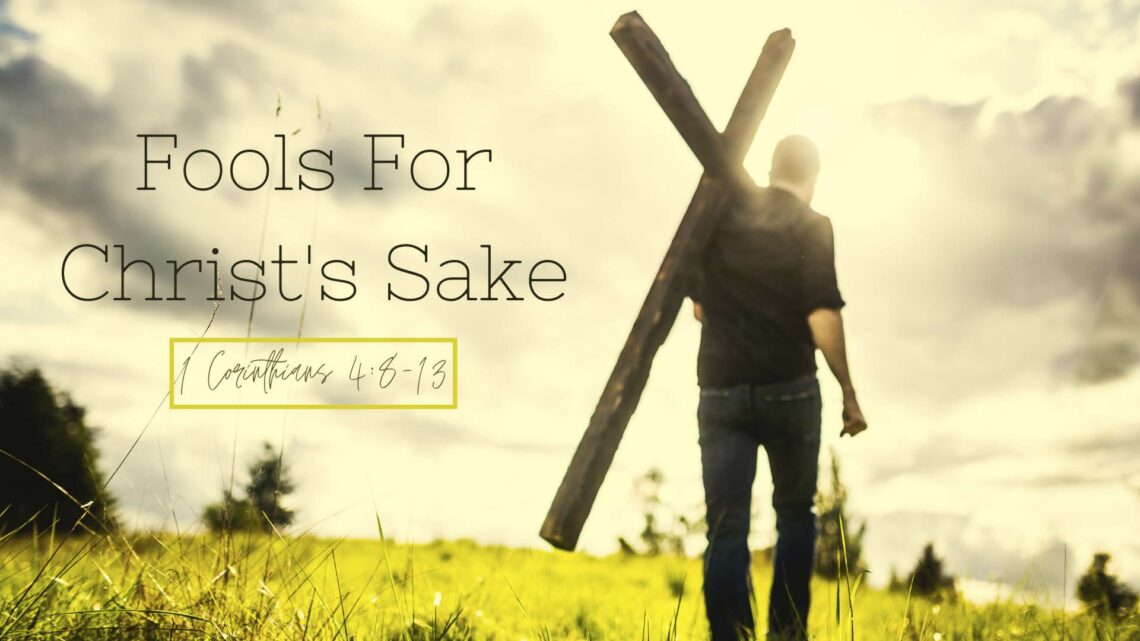 Photo of a man carrying a cross in a field with overlaid words that say Fools For Christ's Sake, 1 Corinthians 4:8-13