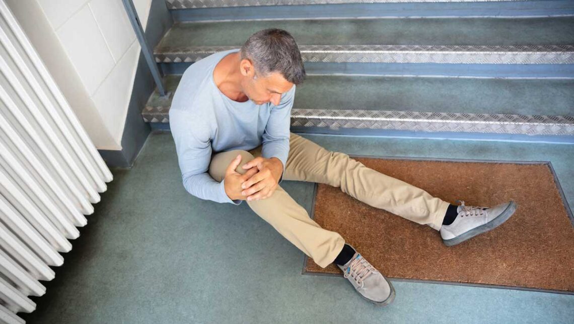 Photo of a man holding his knee at the bottom of stairs following a slip and fall.