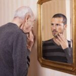 Photo of older man looking in a mirror at his younger self
