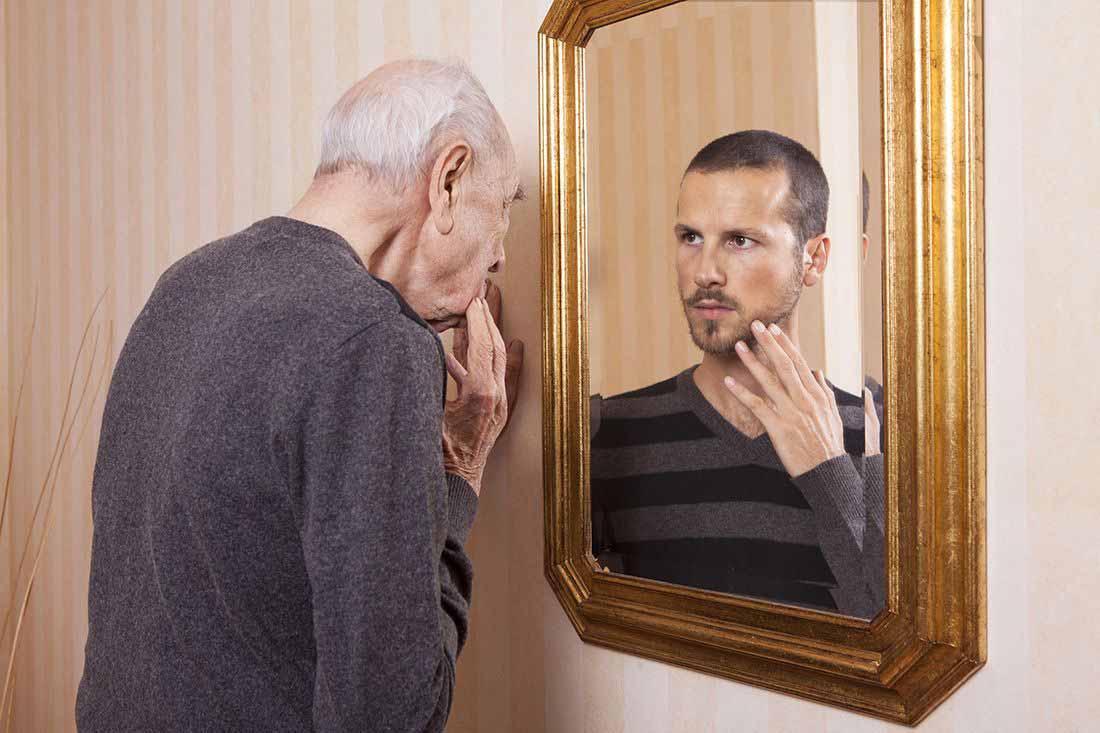 Photo of older man looking in a mirror at his younger self