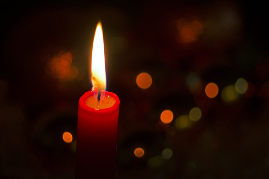 Photo of a single red candle lit against a dark blurry background