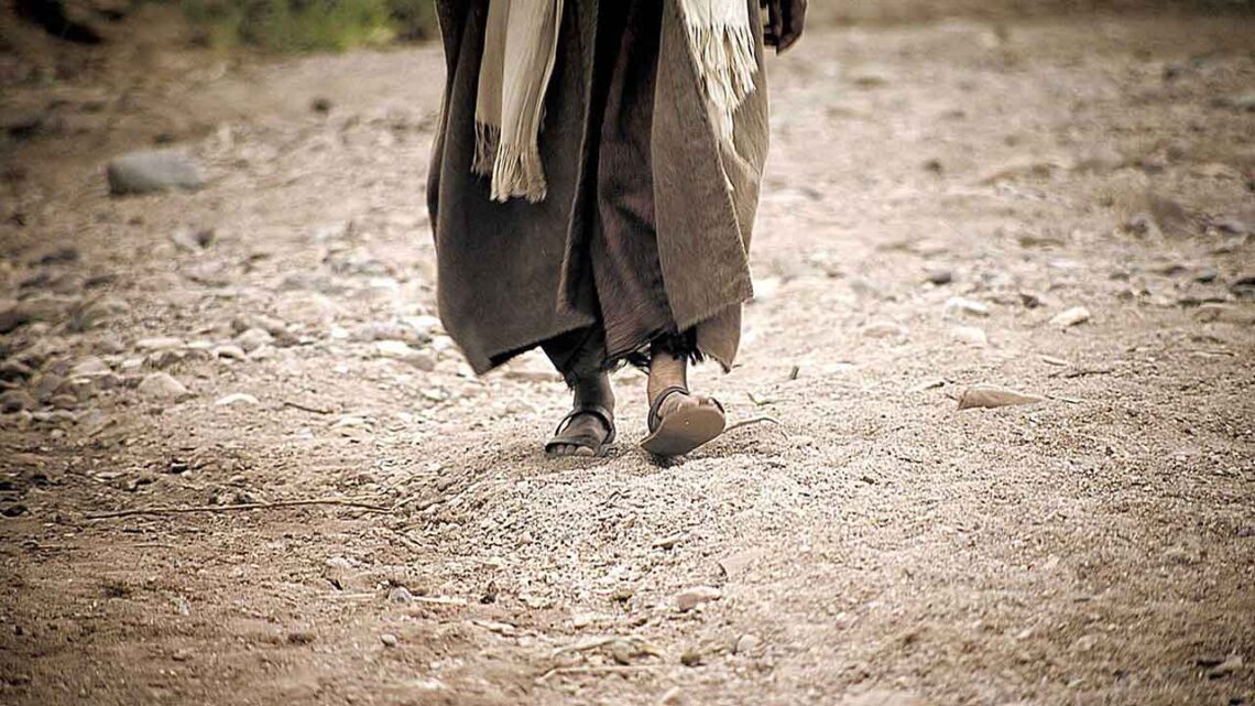 photo of person in robes and sandals walking in sandy soil