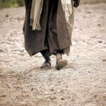 photo of person in robes and sandals walking in sandy soil