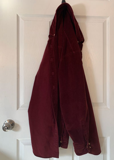 photo of a long-sleeved, burgundy, heavy corduroy shirt hanging on a coat hanger on a door