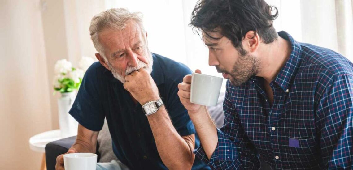 photo of an older man and a younger man sitting and talking over coffee