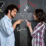 photo of a man and a woman pointing at each other in an argument against a black chalkboard background with various doodles drawn on it