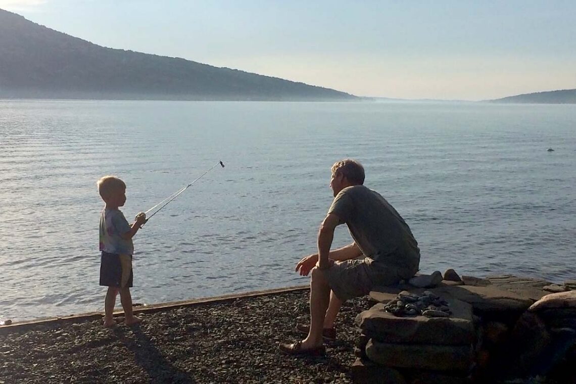 photo of grandfather advising grandson who is fishing on a lake shore